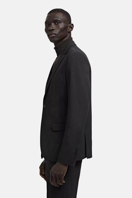 Blazer noire MANGO à un bouton, poches à rabat et quatre boutons de manchettes, portée par un homme avec un col roulé foncé.