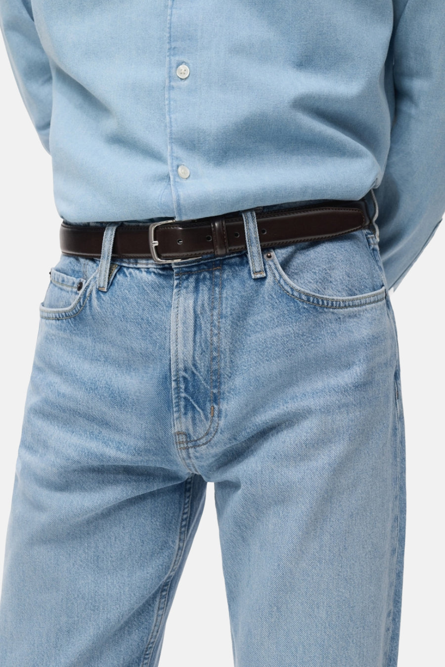 Lichtblauwe straight jeans van MANGO, gecombineerd met een bruine leren riem en een lichtblauw overhemd.

