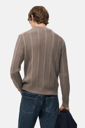 Bruine trui met ronde hals van MANGO, met een ribbelstructuur op de rug en een donkerblauwe jas in de hand.
