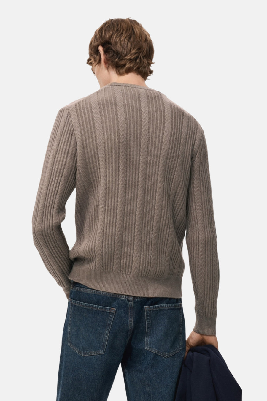 Bruine trui met ronde hals van MANGO, met een ribbelstructuur op de rug en een donkerblauwe jas in de hand.
