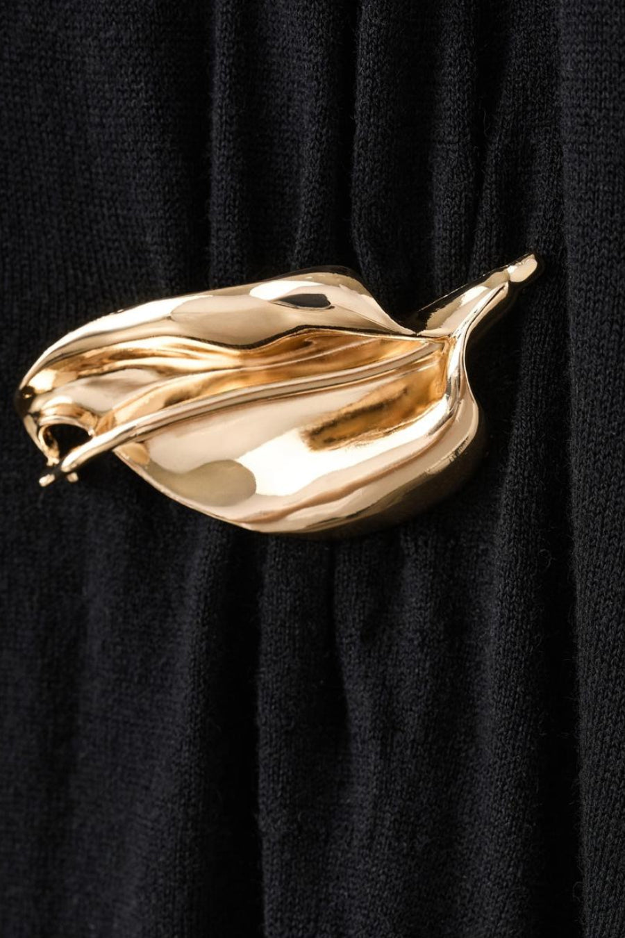 Robe sans manches noire de MANGO, avec une broche dorée brillante en forme de feuille.
