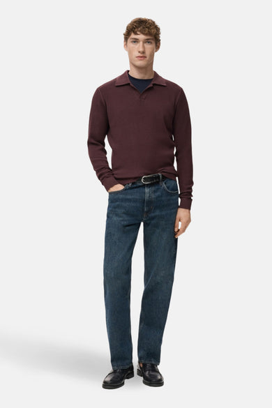 Bordeaux trui met V-hals van MANGO, gedragen met een donkerblauwe top en jeans met een riem.
