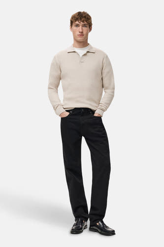 Pull beige à col V de MANGO, avec des manches longues, porté avec des jeans noirs et des loafers en cuir.