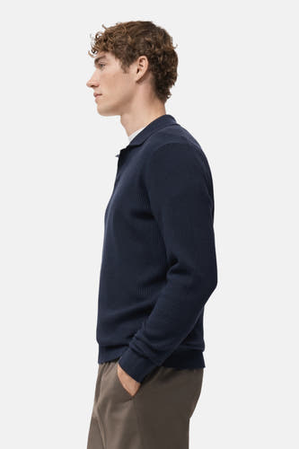 T-shirt bleu à col V de MANGO, avec structure en côtes, porté avec un pantalon marron, en vue latérale.
