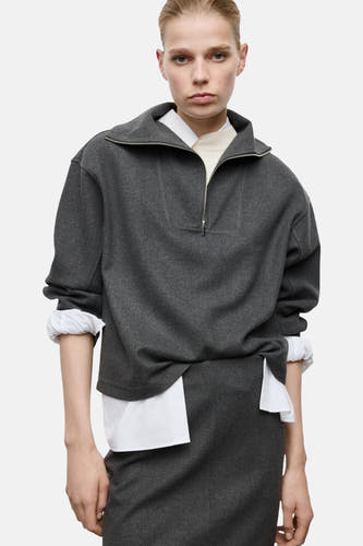 Grijze sweater van MANGO, met een korte ritssluiting en lange mouwen met witte manchetten.