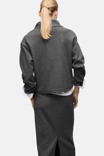 Grijze sweater van MANGO, met lange mouwen en een kraag, gedragen met een grijze rok en een wit overhemd, gezien van achteren.
