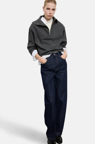 Grijze sweater van MANGO, met een halve rits, gedragen over een wit overhemd en donkere jeans.
