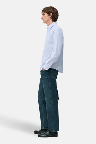 Chemise bleue à manches longues de MANGO, portée avec des jeans foncés et des loafers noirs, vue de dos.