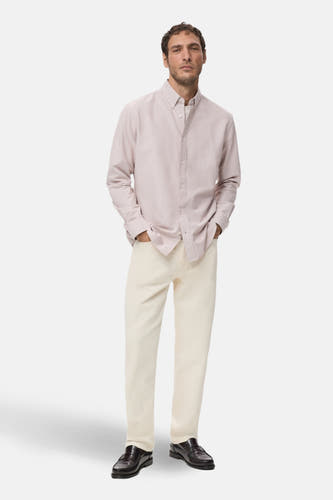 Chemise de homme rose M MANGO avec des manches longues, portée avec un pantalon crème et des loafers en cuir.
