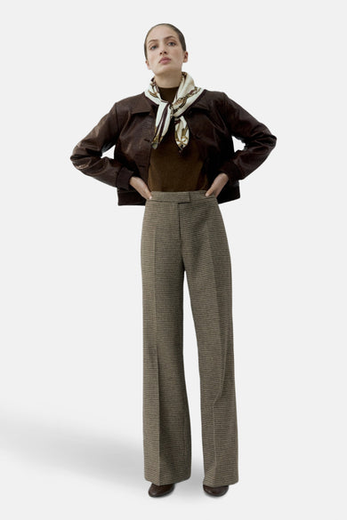 Multikleurige broek van MANGO, met een houndstooth-patroon en wijde pijpen, gecombineerd met een bruine leren jack en een zijden sjaal.