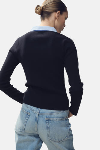 Blauwe trui met V-hals van MANGO, met lange mouwen en een lichtblauwe blouse eronder, achterkant.
