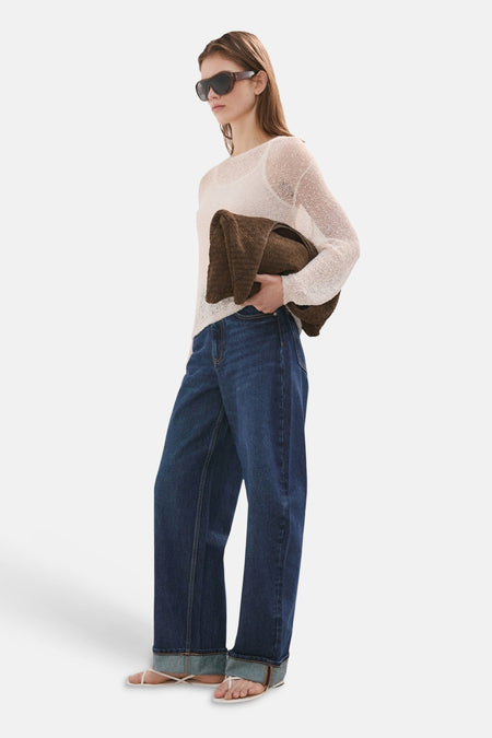 Donkerblauwe denim jeans van MANGO, met wijde pijpen en omgeslagen zoom, gedragen met een losgebreide trui en slippers.
