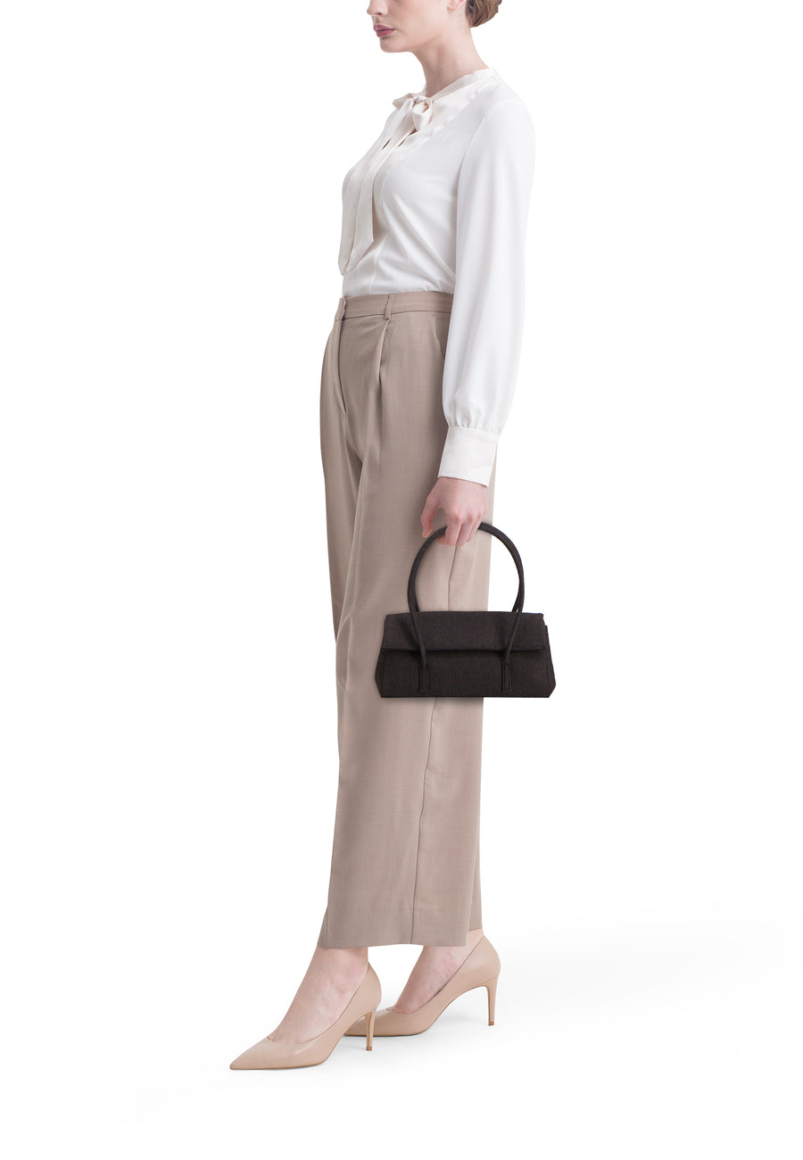 Sac à bandoulière en denim bleu marine de MANGO, porté avec un pantalon beige, une blouse blanche et des talons beiges.