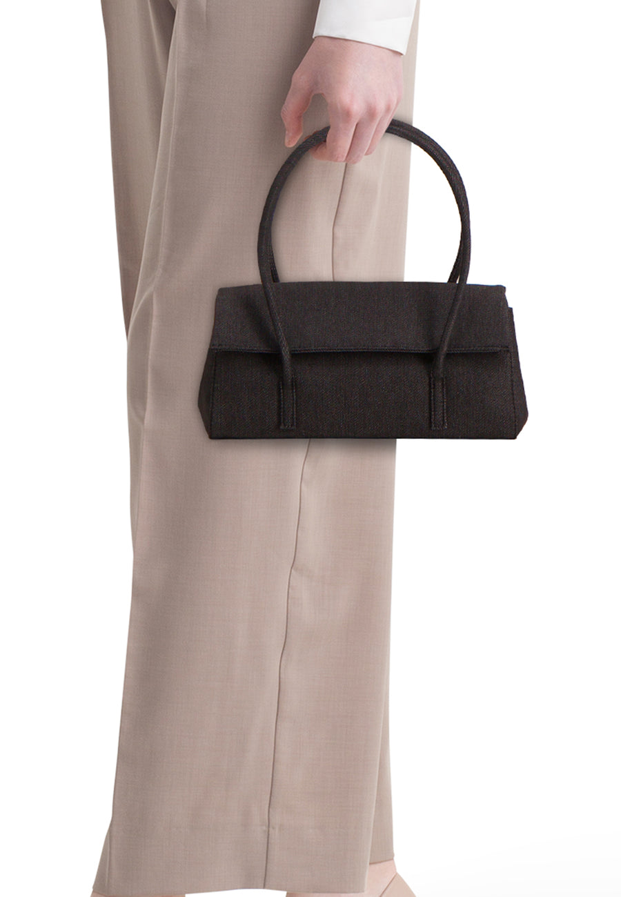 Sac à bandoulière en denim bleu marine de MANGO, avec de courtes anses, porté avec un pantalon beige et une blouse blanche.