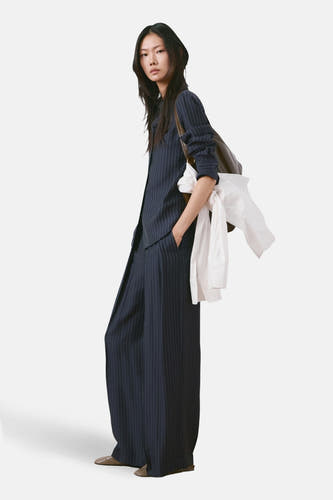 Pantalon bleu MANGO, à rayures craie et jambes larges, combiné avec une chemise rayée assortie et une chemise blanche sur l'épaule.