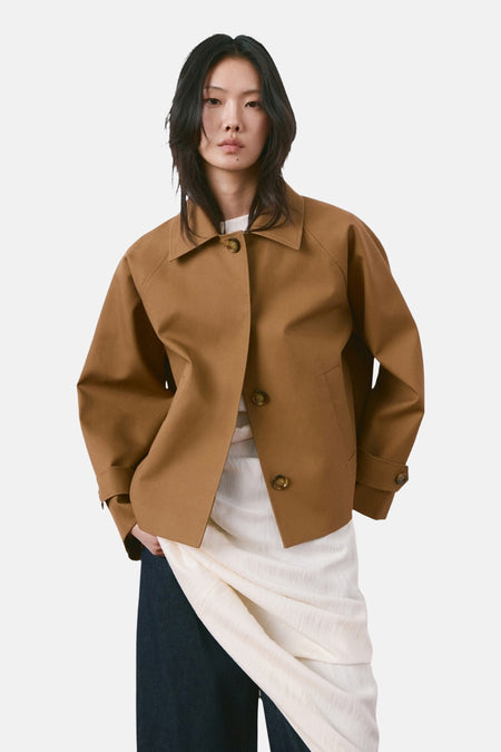 Bruine korte jas van MANGO, met lange mouwen en knoopsluiting, gedragen met een witte top en donkere broek.
