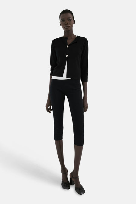 Gilet noir de MANGO, porté sur une chemise blanche et associé à un legging noir et des talons.