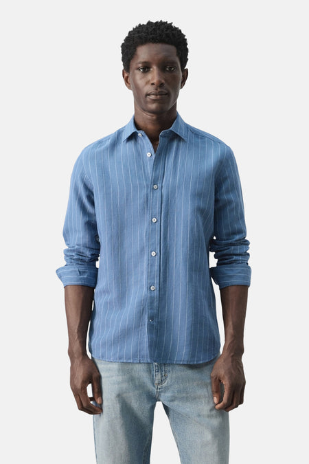 Chemise rayée bleue de MANGO, vue de dos avec les manches retroussées et un jean.