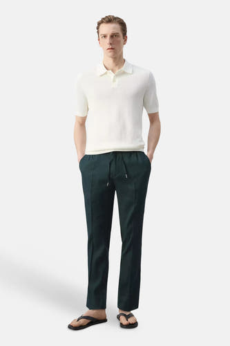 Donkergroene broek van MANGO met trekkoord en verticale vouwen, gestyled met wit poloshirt en zwarte slippers.