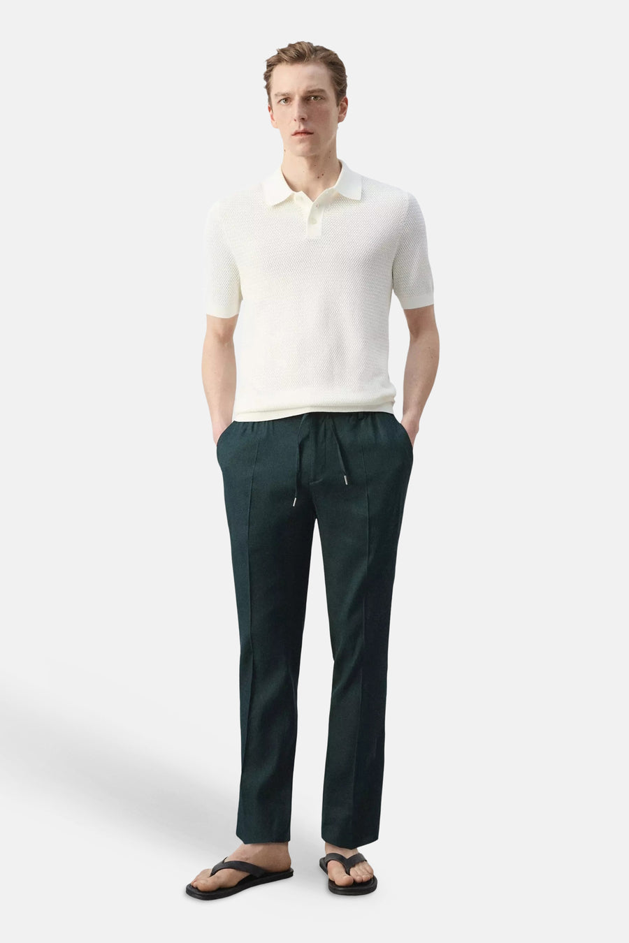 Donkergroene broek van MANGO met trekkoord en verticale vouwen, gestyled met wit poloshirt en zwarte slippers.