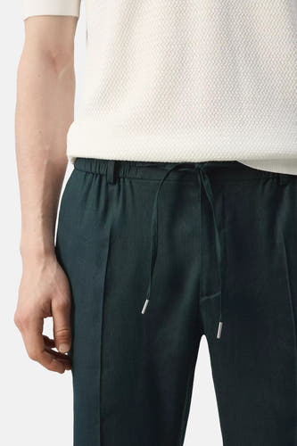 Groene broek van MANGO met trekkoord taille, zilveren aglets en gedragen met een wit gestructureerd T-shirt.