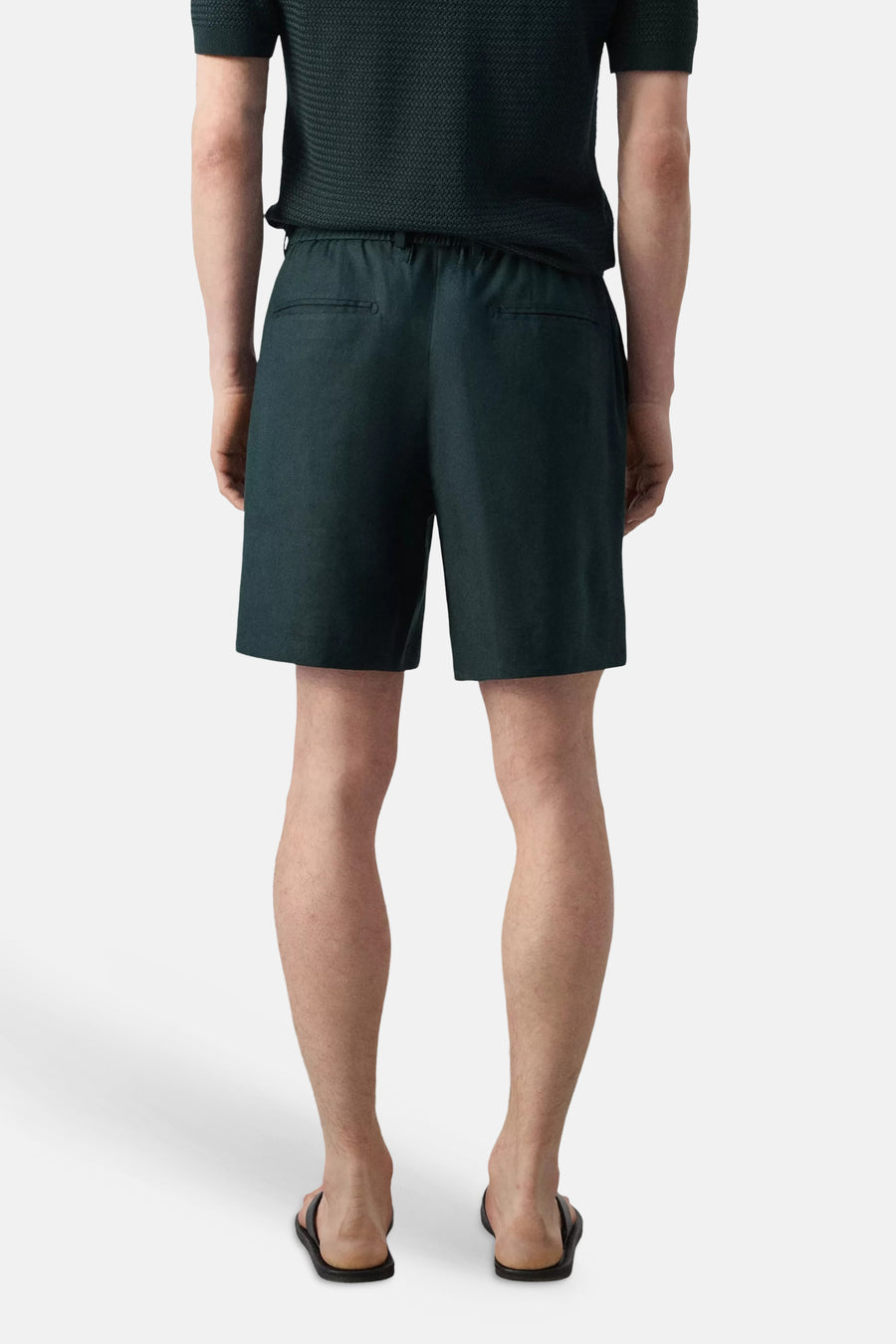 Groene Bermuda's van MANGO, achterkant met twee zakken, model draagt donkergroen shirt en slippers