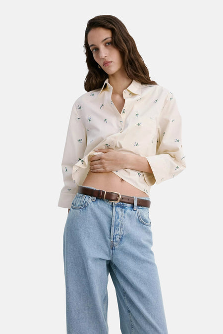 Crèmekleurige blouse met lange mouwen en kleine bloemenprint van MANGO, gekreukt en geknoopt, gedragen met lichtblauwe jeans en bruine riem, lifestyle shot.