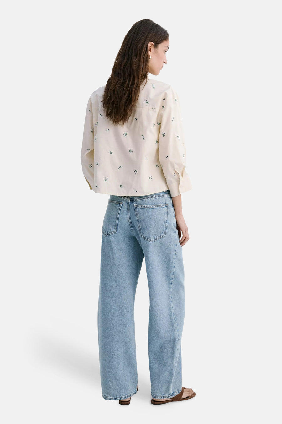 Crèmekleurige blouse met lange mouwen en kleine groene bloemmotieven van MANGO, gedragen van achteren met lichte jeans en sandalen