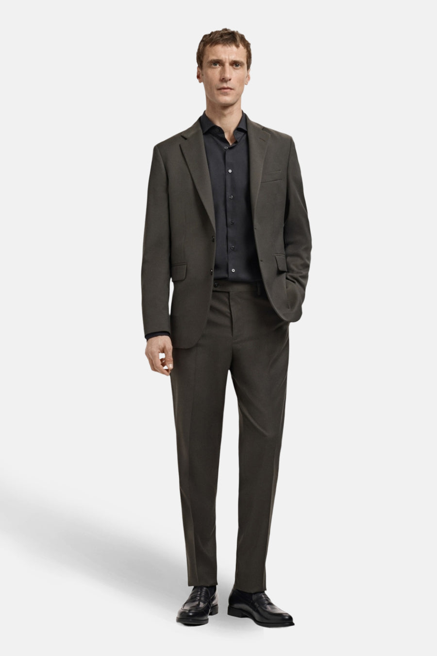 Man in grijsbruin pak met zwart overhemd en schoenen.