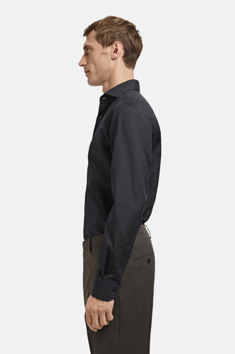 Man in zwart overhemd en groene broek, zijprofiel.
