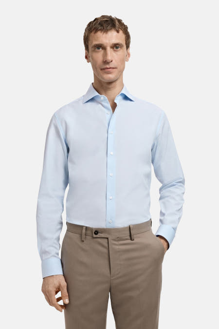 Chemise bleue à manches longues de MANGO, portée sous un manteau brun.