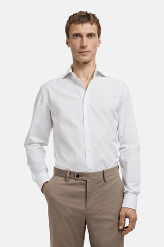 Man in wit overhemd en beige pantalon, staand.
