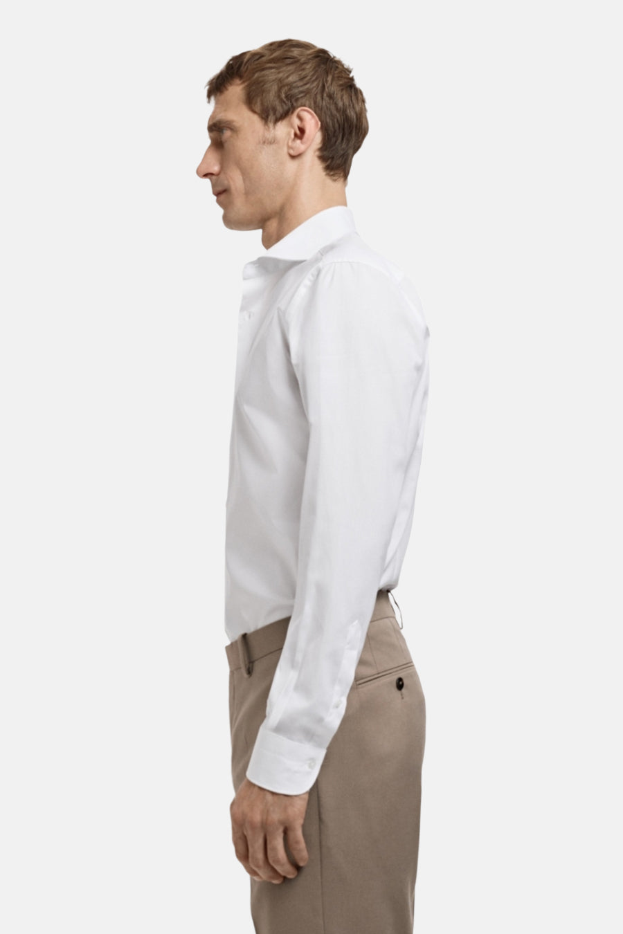 Een man in een wit overhemd en beige broek, in profiel.