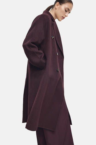 Lange rode jas van MANGO, met lange mouwen, knoopsluiting en zijzakken, gedragen met een rode broek.
