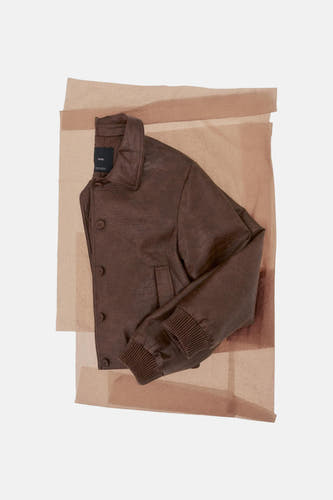 Bruine korte jas van MANGO, weergegeven op laagjes van doorschijnend papier, met een gekreukte textuur en geribbelde manchetten.
