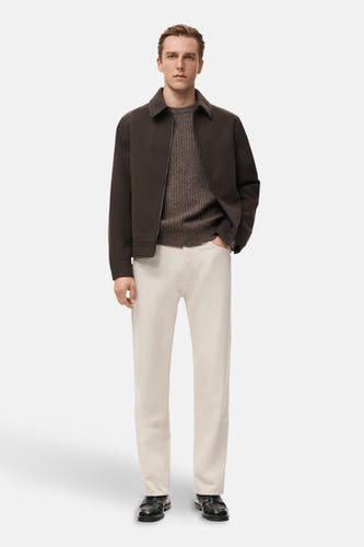 Jean en denim blanc cassé droit de MANGO, associé à une chemise brune et un manteau brun foncé. Modèle debout.