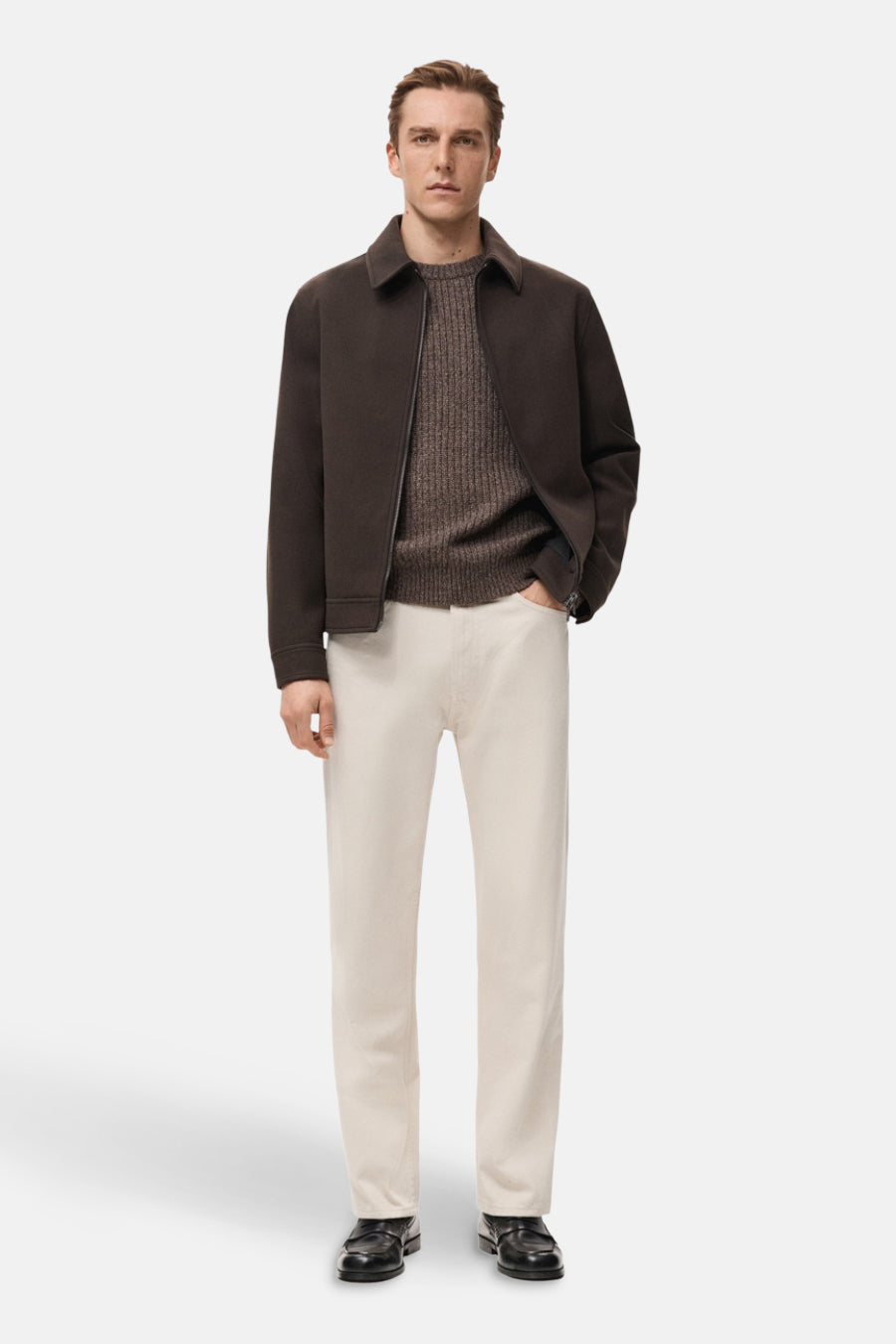 Jean en denim blanc cassé droit de MANGO, associé à une chemise brune et un manteau brun foncé. Modèle debout.