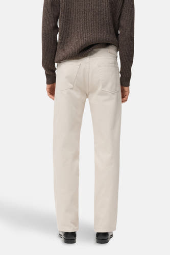 Rechte jeans van off-white denim van MANGO, met achterzakken, gecombineerd met een bruine trui en zwarte schoenen, gezien van achteren.
