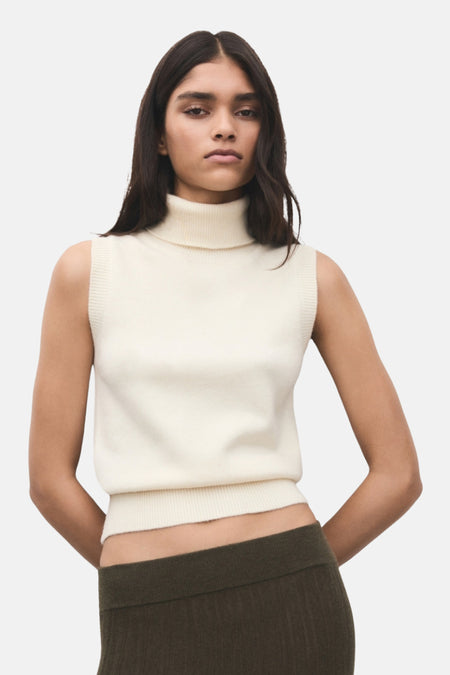 Model draagt mouwloze coltrui en groene rok.