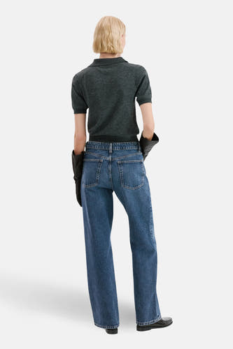 Donkerblauwe straight jeans van MANGO, gezien van achteren, gecombineerd met een grijze polo en zwarte leren handschoenen.