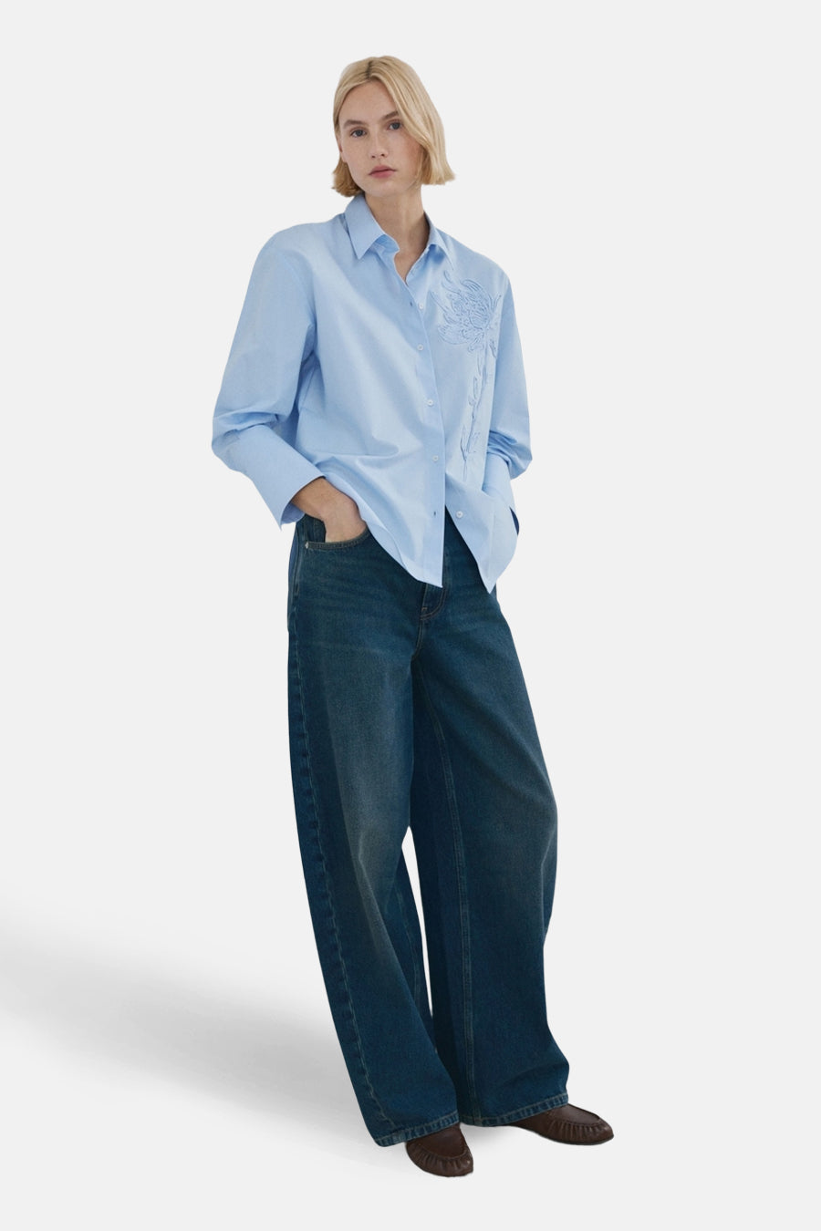 Blauw overhemd met lange mouwen van MANGO, met subtiel bloemmotief aan de voorzijde, gecombineerd met wijde jeans en bruine mocassins.
