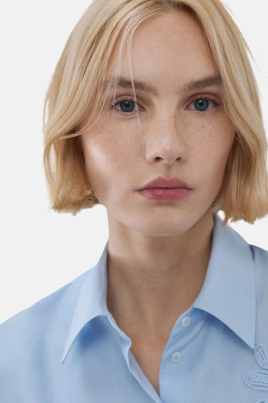 Blauw, lange mouwen overhemd van MANGO, close-up van een model met blonde bob en blauwe ogen.