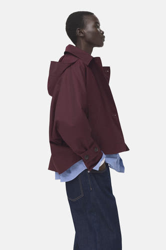 Bordeaux jas van MANGO, met kap, gedragen over een gestreept overhemd en donkere jeans.