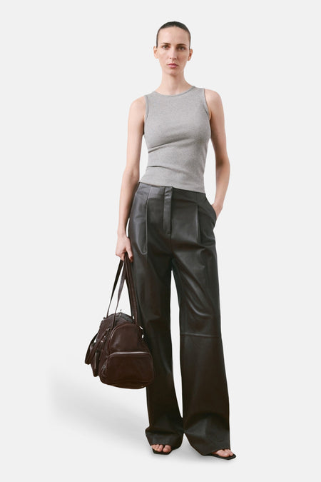 Haut grise de MANGO, combinée avec un pantalon en cuir ample et un sac marron.