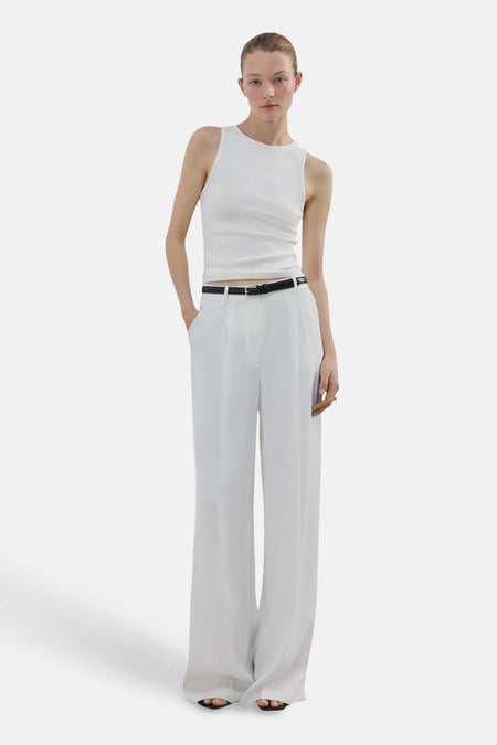 Débardeur blanc de MANGO, porté avec une ceinture noire et un pantalon blanc évasé.