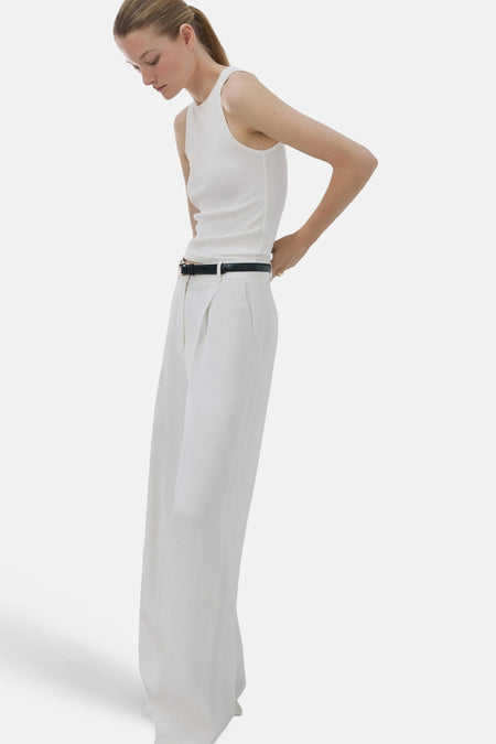 Débardeur blanc de MANGO, avec un col rond et porté avec une ceinture noire et un pantalon blanc.