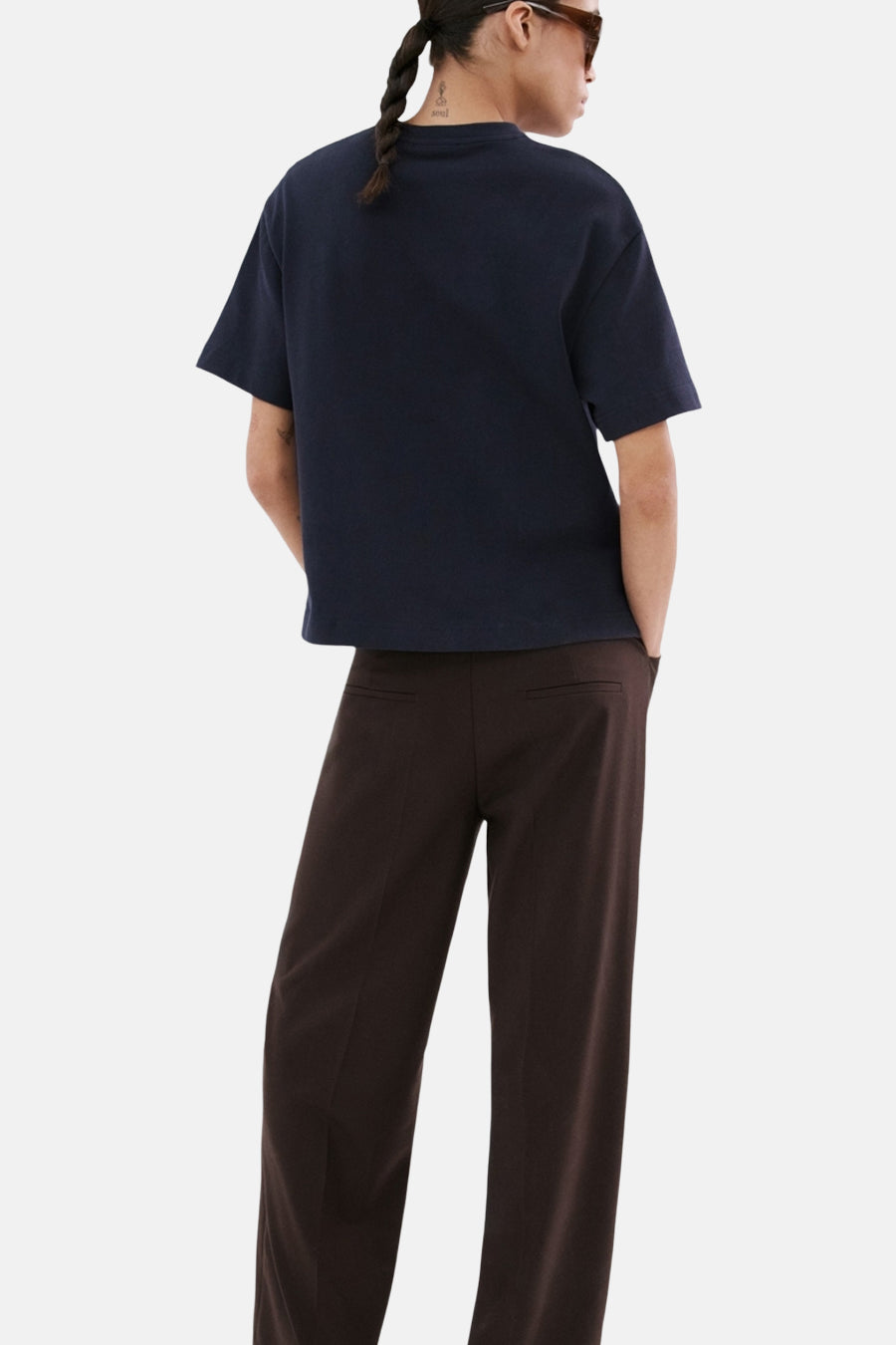 Blauw T-shirt van MANGO, gezien van achteren, met bruine pantalon en gevlochten haar.