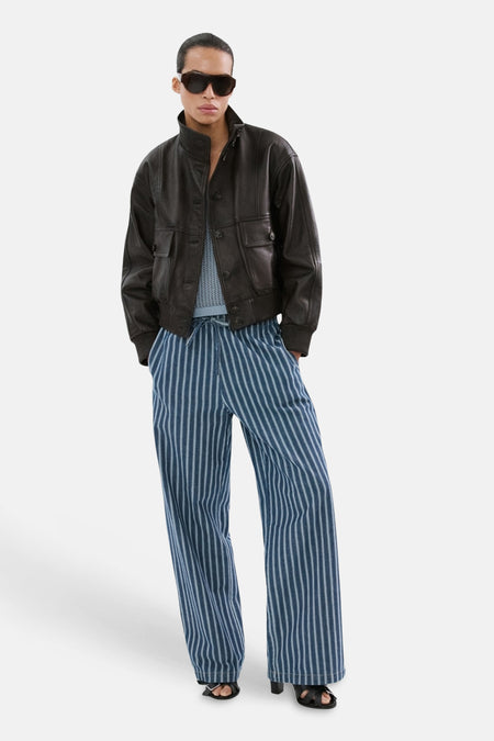 Blauwe broek van MANGO, met verticale strepen, gecombineerd met een leren jas en zonnebril.
