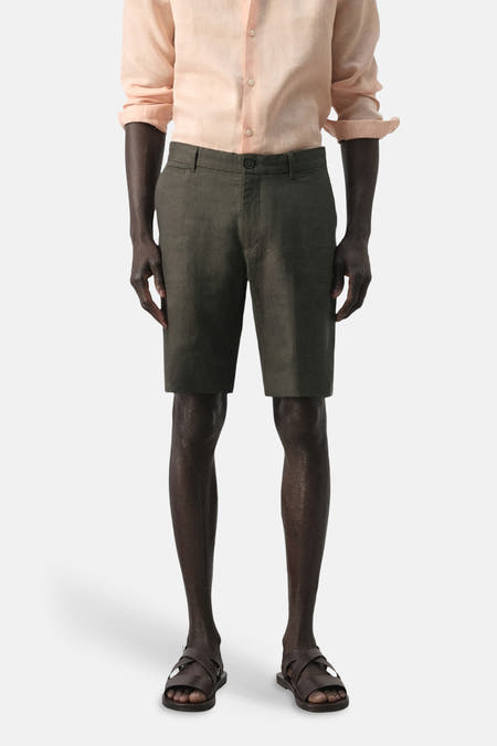 Kaki bermuda van MANGO, met een klassieke pasvorm en subtiele textuur, gecombineerd met een lichtroze overhemd en bruine sandalen.