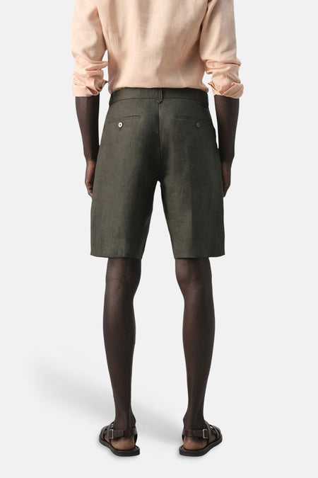 Kaki bermuda van MANGO, gezien van achteren, met een lichtroze linnen overhemd en bruine sandalen.
